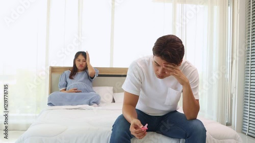 Husband sits with head lowered, stressed, holding condom, looking depressed because he can't have sex with his pregnant wife : Concept preventing impact during pregnancy.