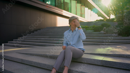 Caucasian ill sick unwell exhausted businesswoman mature mid age tired business woman sit on stairs city outdoor feel discomfort blurry vision eye strain taking off glasses headache full length shot photo