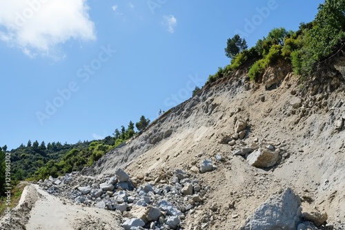 A destructive landslide burying a mountain road, with rocks and debris tumbling down the slope.
