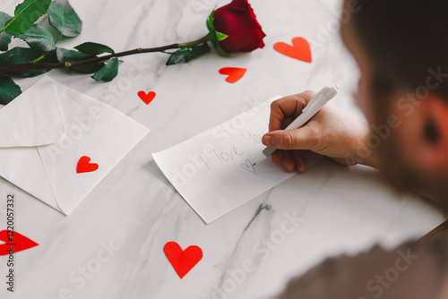 Cuadro en lienzo A man writes a heartfelt note saying I love you on an envelope, surrounded by red hearts and a single rose on a marble table, creating a romantic atmosphere