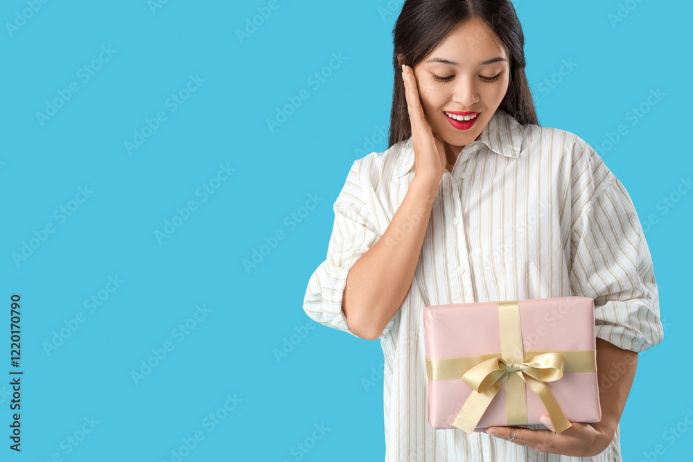 Beautiful surprised Asian woman with gift box on blue background Beautiful surprised Asian woman with gift box on blue background
