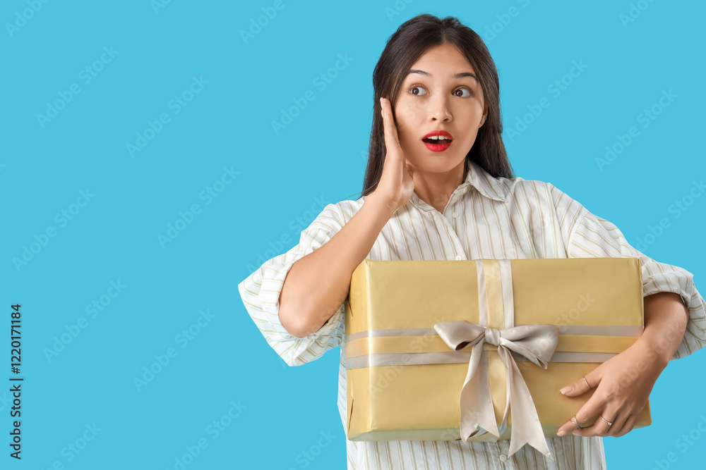 Beautiful shocked Asian woman with gift box on blue background Beautiful shocked Asian woman with gift box on blue background