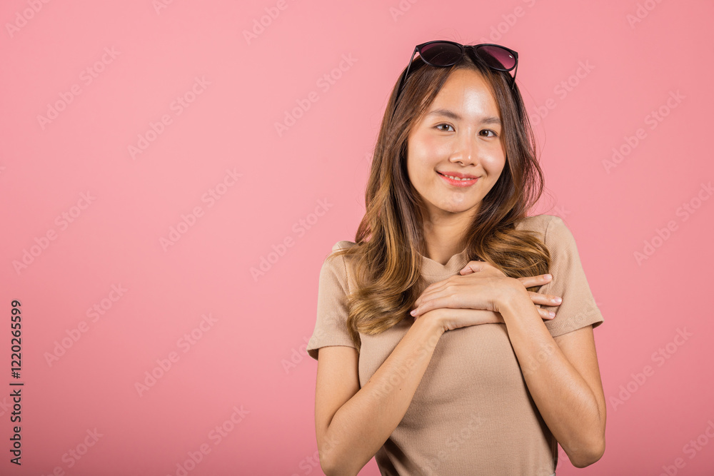 Beauty Asian young woman touching her chest for thanking in studio shot isolated on pink background, happy charming female smiling hold hands chest near heart honest with grateful gesture