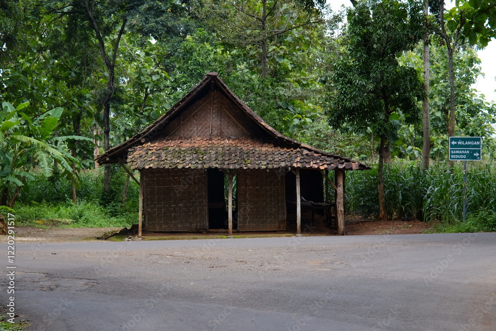 A rustic bamboo house stands by a quiet rural road, surrounded by lush greenery, showcasing traditional architecture A rustic bamboo house stands by a quiet rural road, surrounded by lush greenery, showcasing traditional architecture