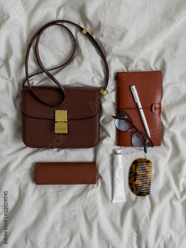 Women's accessories on the bed - cross body bag, glasses, notebook, comb, cream, top view photo