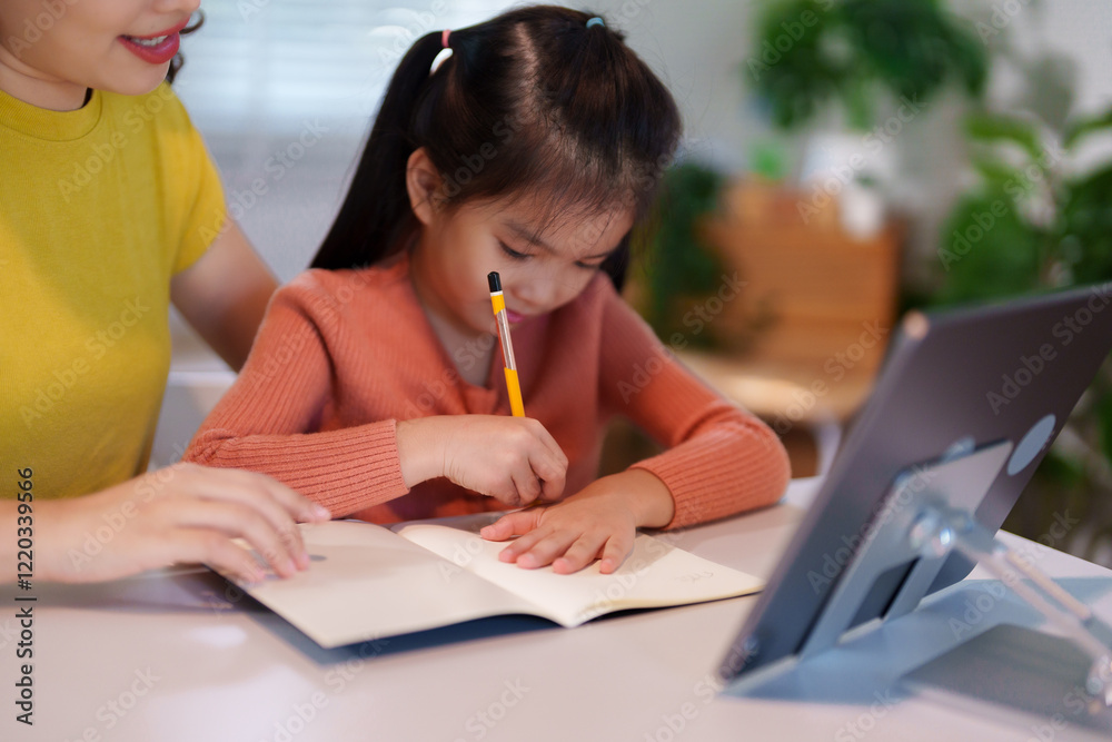 A mother is teaching her young daughter to do homework together at the table, creating a supportive and educational environment. A mother is teaching her young daughter to do homework together at the table, creating a supportive and educational environment.