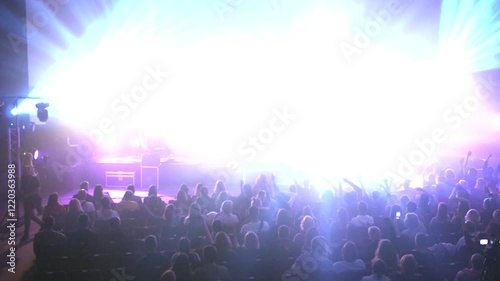 A concert hall alive with the energy of a live performance. A vibrant spectacle of light and sound, captivating the crowd. A rock band is playing on stage. Electric energy fills the venue as the band  photo