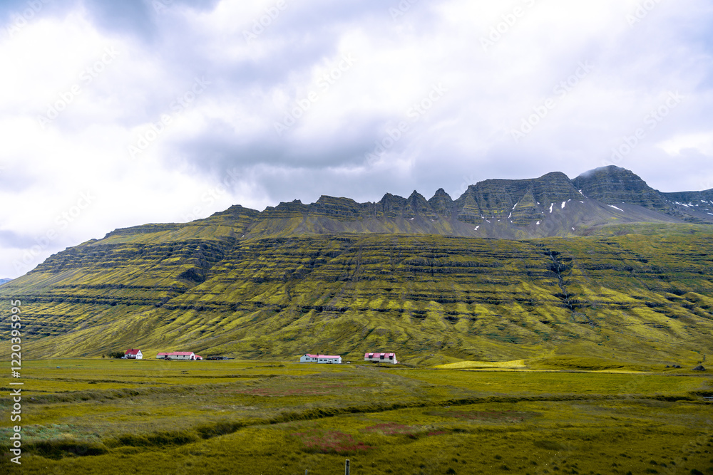Fototapeta premium Near Reydarfjordur, eastern Iceland, a stunning view of high mountains blends seamlessly with a backdrop of dramatic, swirling clouds