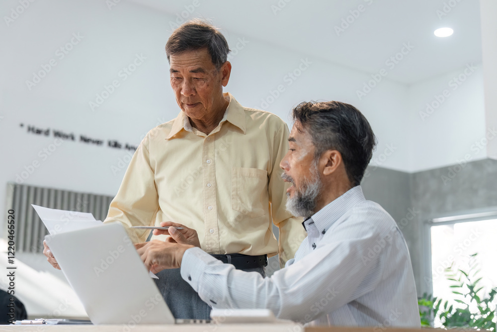 Obraz premium Seasoned businessmen discussing project updates while examining documents in a bright office environment