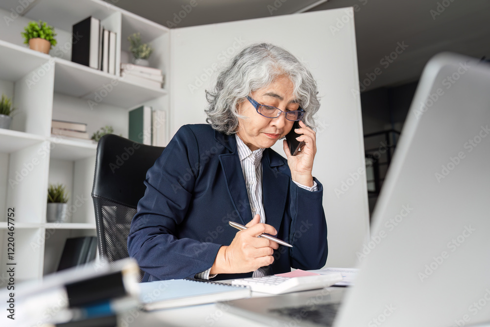 Elderly business woman managing tasks while on the phone in a modern office setting Elderly business woman managing tasks while on the phone in a modern office setting