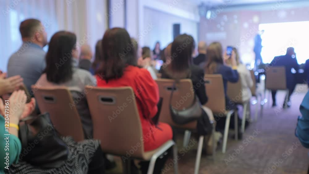 A group of people are sitting in chairs in a room. The chairs are arranged in rows and the people are looking at a screen. Scene is serious and focused A group of people are sitting in chairs in a room. The chairs are arranged in rows and the people are looking at a screen. Scene is serious and focused