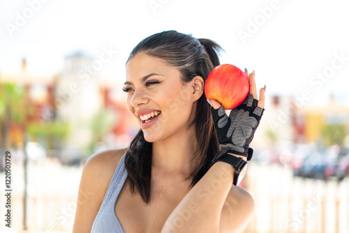 Young pretty sport woman at outdoors holding an apple with happy expression photo