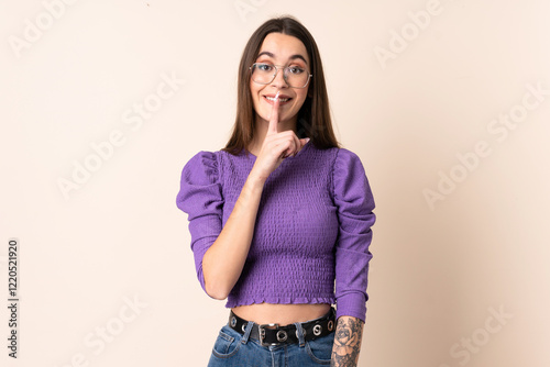 Young woman over isolated beige background showing a sign of silence gesture putting finger in mouth photo