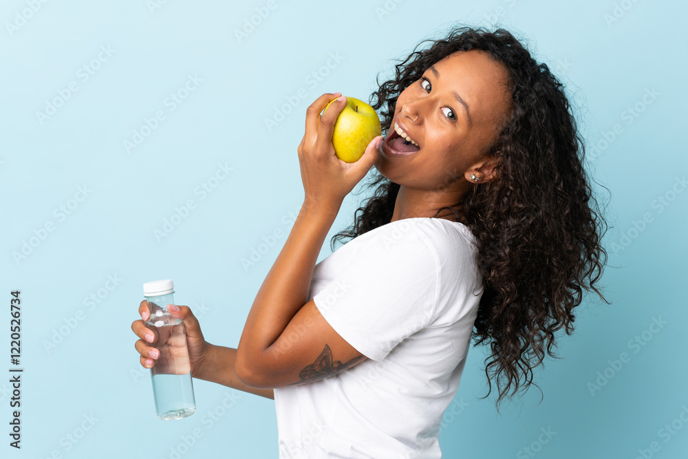Teenager cuban girl isolated on blue background with an apple and with a bottle of water Teenager cuban girl isolated on blue background with an apple and with a bottle of water