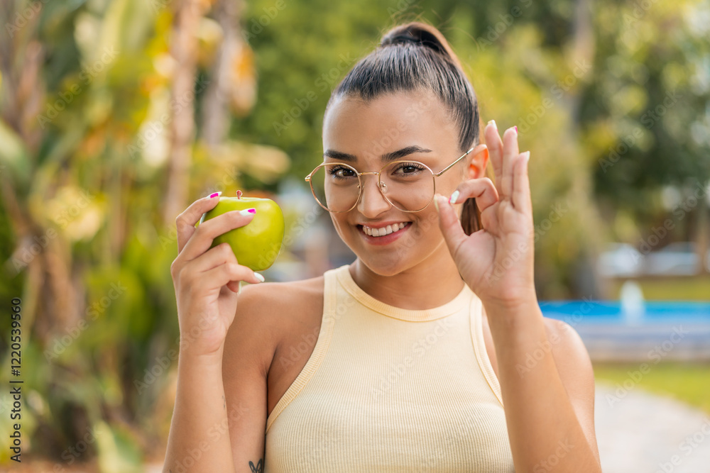 Young pretty woman with an apple at outdoors showing ok sign with fingers Young pretty woman with an apple at outdoors showing ok sign with fingers
