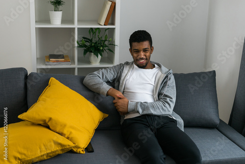 Cheerful curly haired ethnic african american male in casual clothes resting at home on comfortable sofa while watching tv channels or movie during weekend. Tv set, online television and entertiment