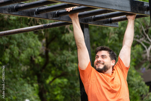 Hombre sonriente entrenando haciendo balanceos en barras. Entrenamiento al aire libre photo