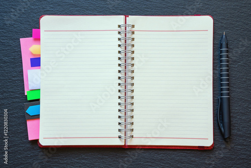 Open spiral bound notebook with blank pages and colorful bookmarks. Dark background, flat lay, copy space