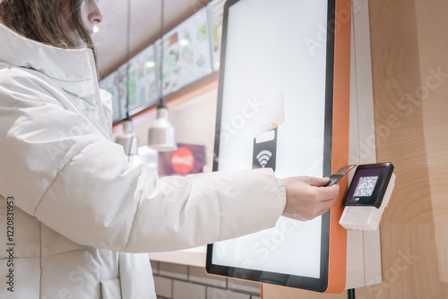 A satisfied customer is using a contactless payment system at a modern fast food kiosk, enjoying convenience, A woman pays with a card for a purchase through a touchscreen terminal for ordering food