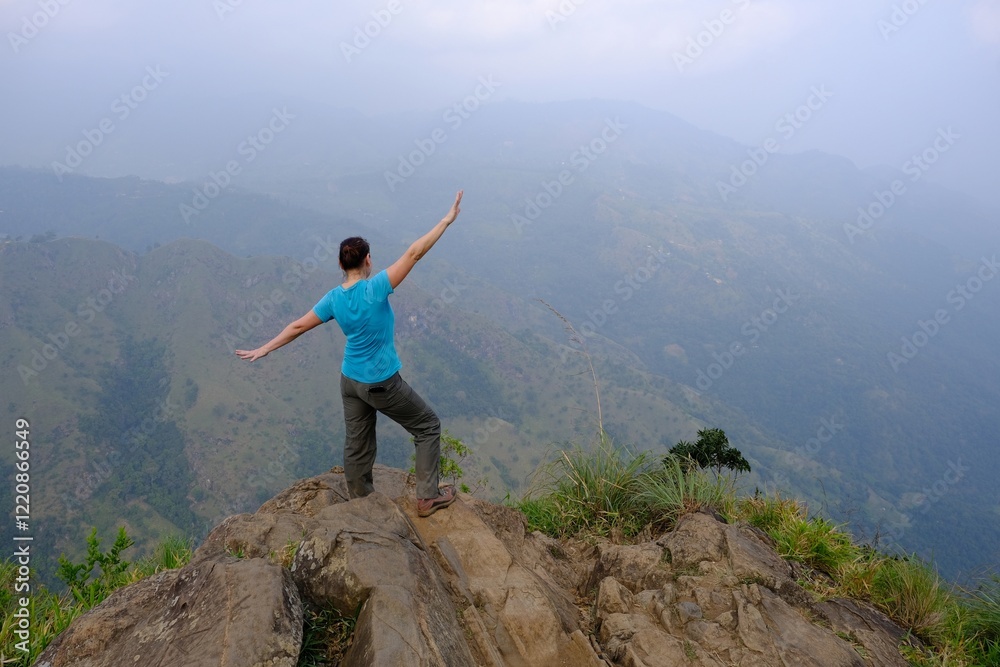 Obraz premium Misty scenery of viewpoint Rock Ella in Sri Lanka with silhouette of standing woman with raised arms in blue shirt.