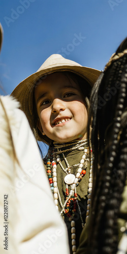 Smiling Child in Traditional Attire with Beaded Necklace Under Clear Blue Sky