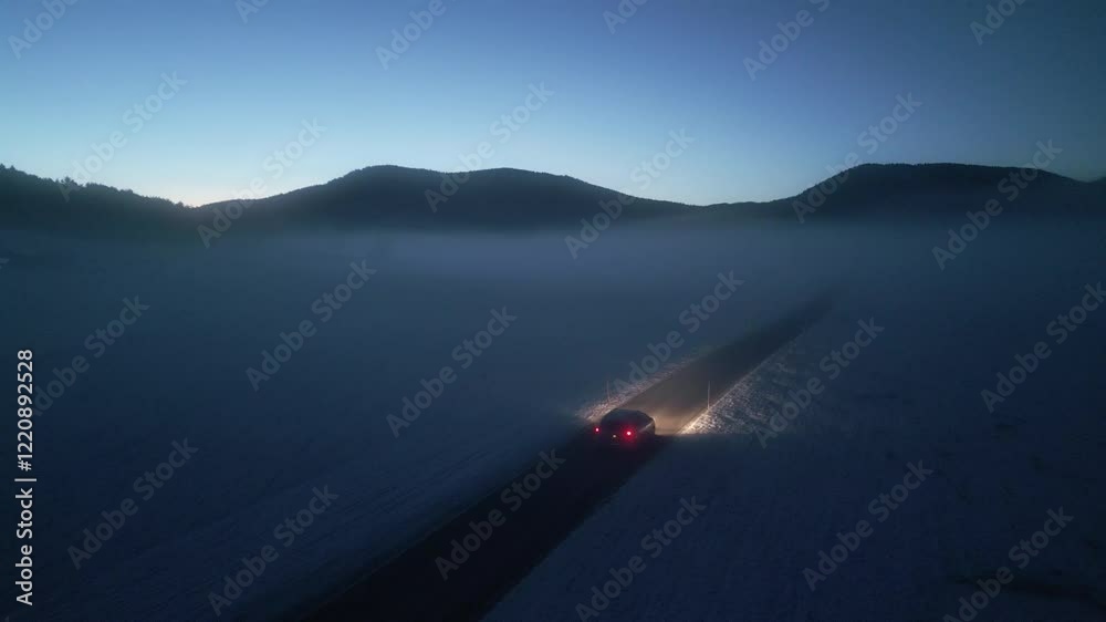 Car riding through dark winter countryside during sunrise aerial tracking shot. Vehicle journey in snowy rural landscape drone view