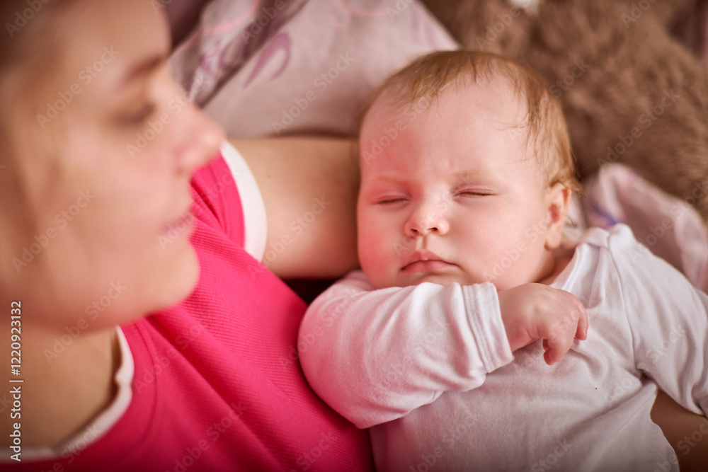 Young blonde woman cradles sleeping baby girl with light hair. Warm lighting, soft background create comforting atmosphere. Pink, beige hues dominate scene Young blonde woman cradles sleeping baby girl with light hair. Warm lighting, soft background create comforting atmosphere. Pink, beige hues dominate scene