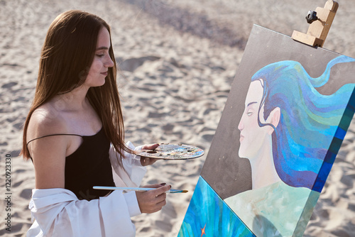 Young female painter creates portrait on sunny beach, blending art with nature. Her serene expression reflects creativity and peace as she mixes vibrant colors on her palette