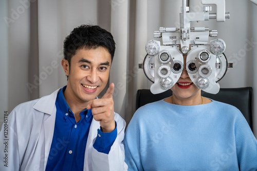 Asian male optometrist performing eye exam senior female woman with phoropter and smiling for patient care