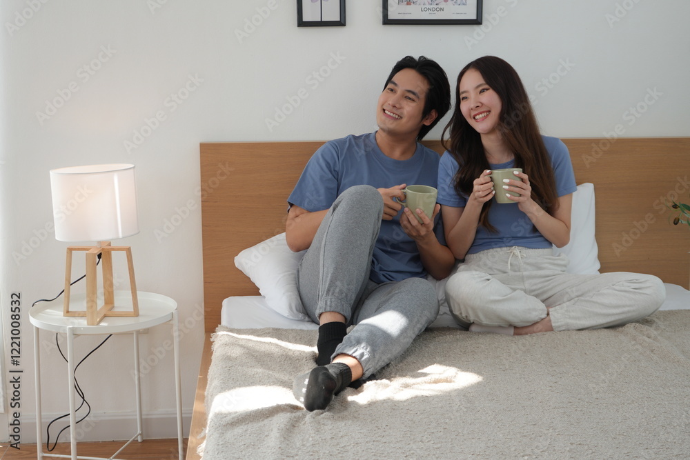 Asian couple husband and wife wearing pajamas wake up early sit talk and drink coffee morning drink drink coffee together refresh on bed make bedroom home family warm