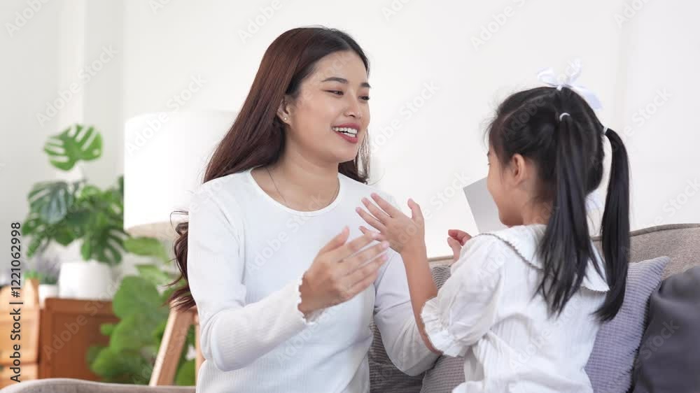 A mother admires a colorful card her young daughter made, showcasing their shared creativity and bonding moment on the couch. A mother admires a colorful card her young daughter made, showcasing their shared creativity and bonding moment on the couch.