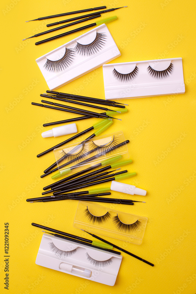 Flat lay composition with false eyelashes, cosmetic products and tools on trendy bright yellow background, concept of lashmakers work place, beauty industry, salon, minimal style