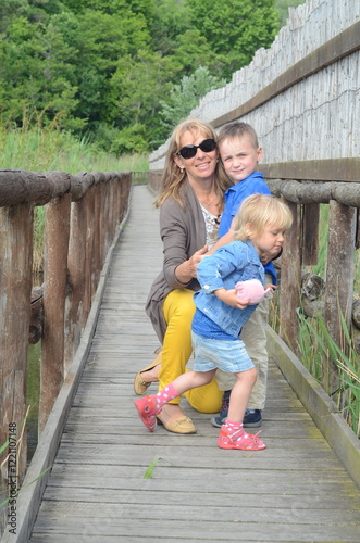 Grandmother with little grandchildren on a wooden path on stilts on the shore of a lake. WWF path as a concept of wildlife conservation photo