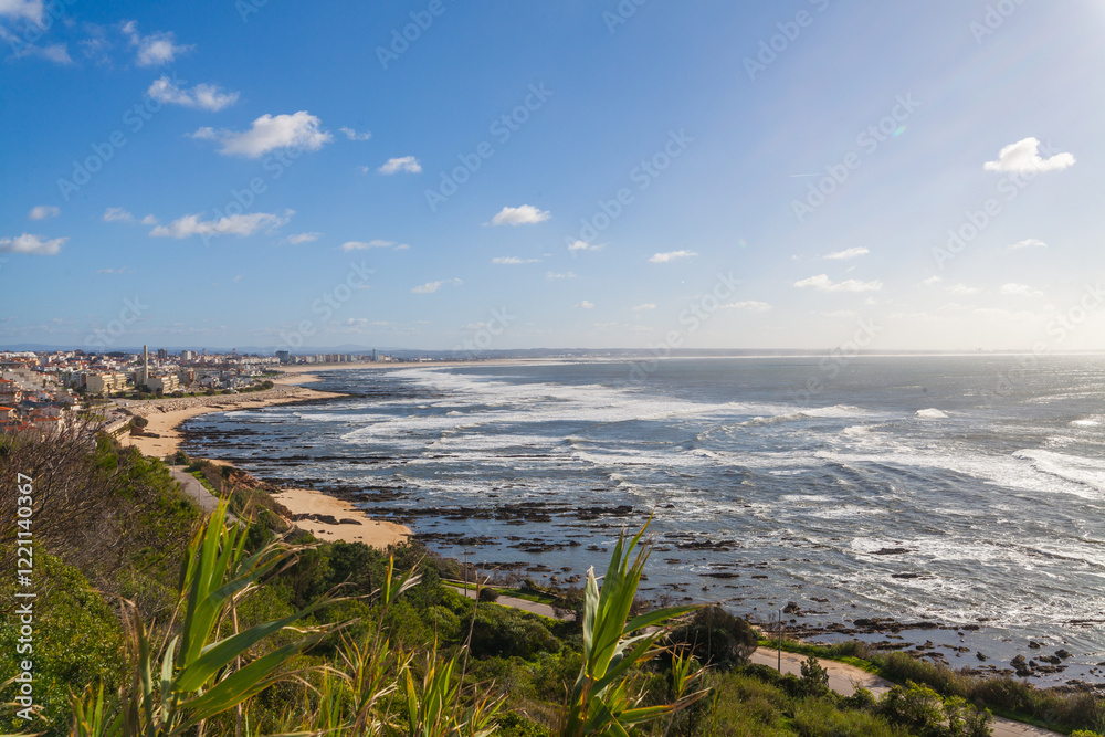A coastal scene with a town bordering a rocky beach, waves crashing on the shore, and a blue sky with scattered clouds A coastal scene with a town bordering a rocky beach, waves crashing on the shore, and a blue sky with scattered clouds