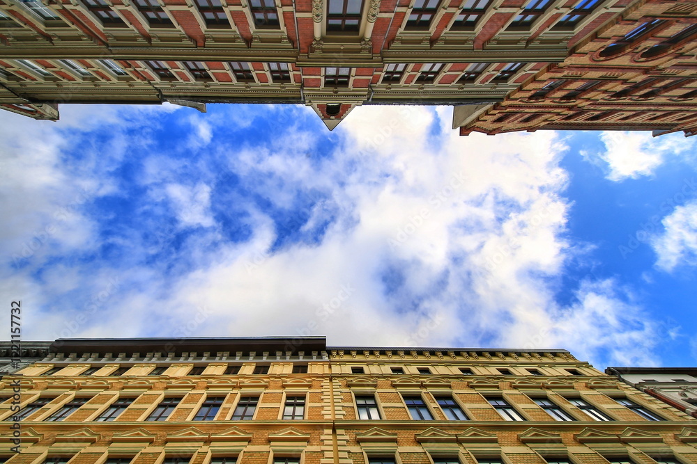 Upward view of historic building facades framing a bright blue sky with scattered clouds Upward view of historic building facades framing a bright blue sky with scattered clouds