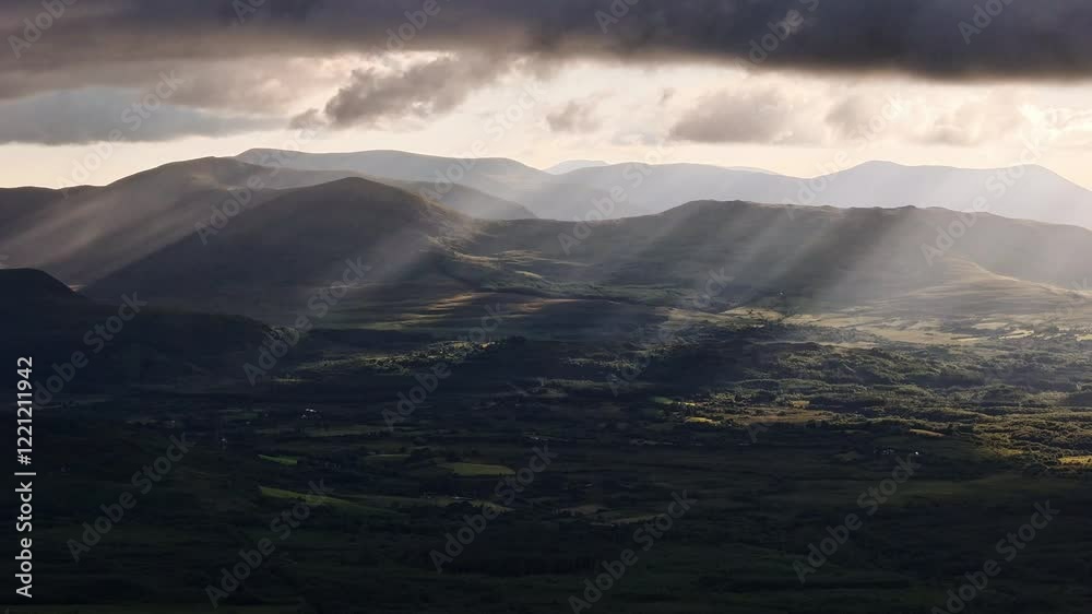 Rolling hills and valleys extend to distant mountains under a partially clouded sky. Sunlight filters through creating light rays. Rolling hills and valleys extend to distant mountains under a partially clouded sky. Sunlight filters through creating light rays.