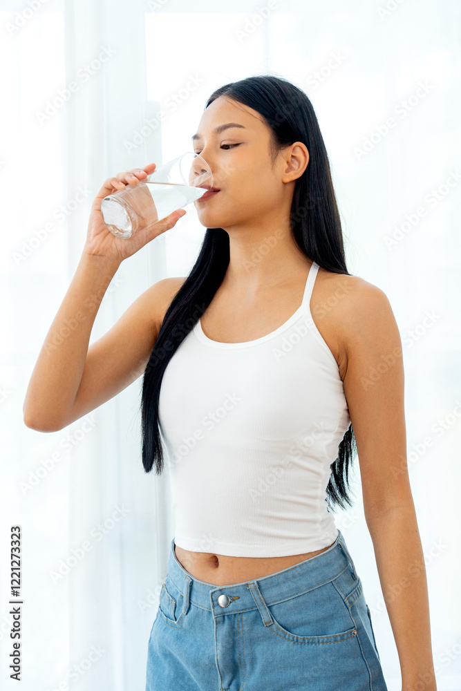 Vertical image of beautiful Asian woman drink water from glass and stand in front of glass window with day light. Vertical image of beautiful Asian woman drink water from glass and stand in front of glass window with day light.
