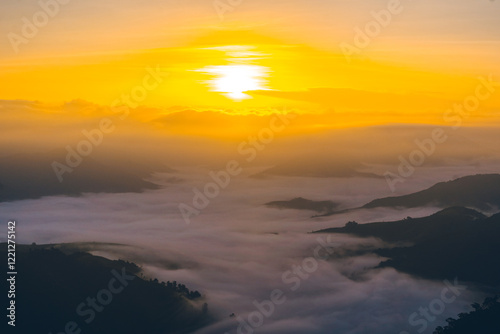 High-angle view of the mountain with fog in the morning in Thailand. The sun rises above clouds in warm tones. The idea for a nature background with copy space. The fog is very thick and fluffy.