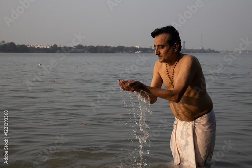 An Indian man taking a holy dip in the river ganges during early morning. he is chest deep submerged in water and is offering prayers to god.