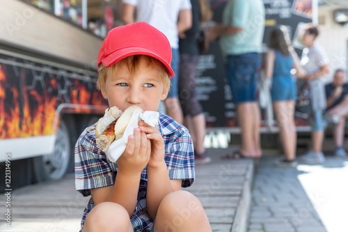 Foto Cute adorable pensive little boy kid enjoy eating hot dog sausage in bread near street cafe stall outdoors