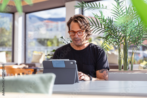 A businessman with causal outfit s sitting at a table working with a tablet in front of him