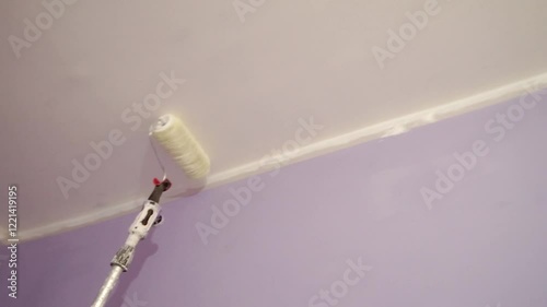 Roller with extension pole applies white paint to ceiling. Interior home improvement. painting services. 