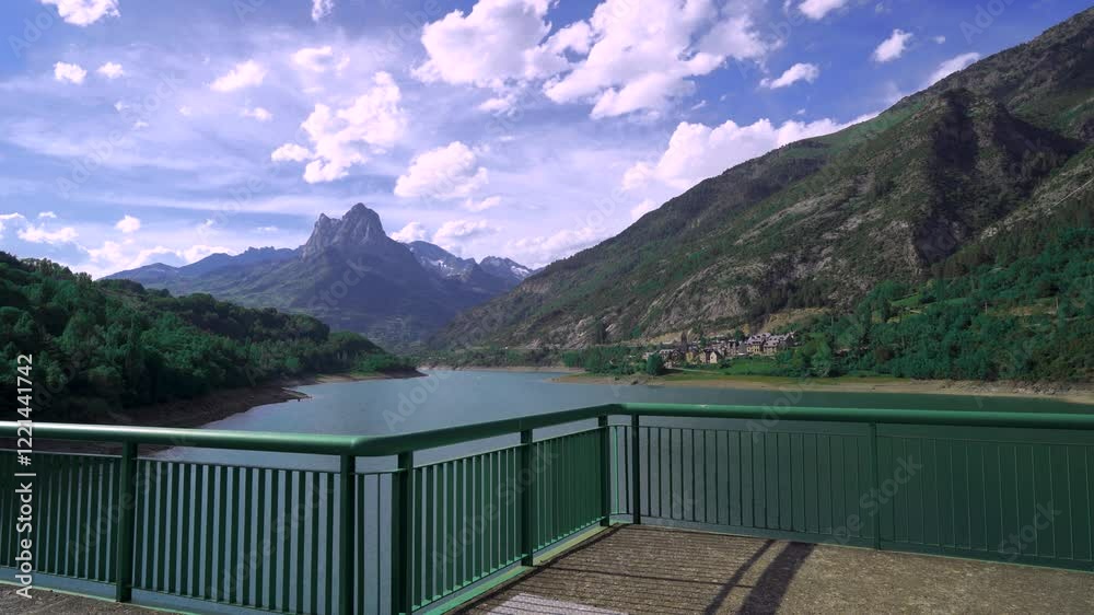 Paisaje de un lago con montañas al fondo y un pueblo un día soleado con cielo azul, nubes y con movimiento de cámara. Desde los Pirineos, Lanuza, Sallent de Gállego, Huesca, Aragón, España, Europa.