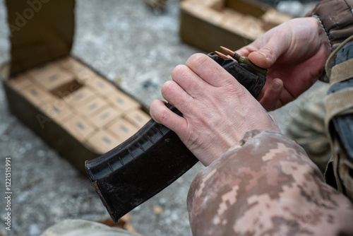 Close-up image of two Ukrainian soldiers reloading weapons and unpacking ammunition on the frozen ground. The worn rifle and dusty gear illustrate the harsh realities of front-line service.