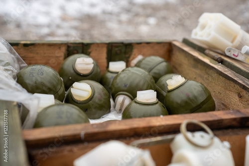 Military grenades stored in a wooden crate at an outdoor location during daylight