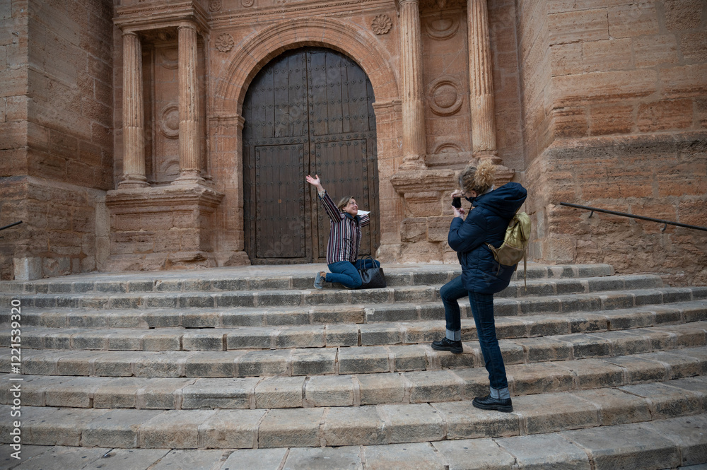 A middle-aged woman smiling while posing on stone steps in front of a large wooden church door, captured by her friend during a winter cultural tour A middle-aged woman smiling while posing on stone steps in front of a large wooden church door, captured by her friend during a winter cultural tour