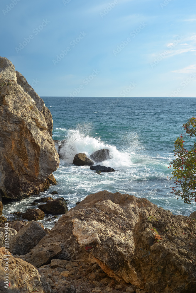 Waves of the Black Sea crash on a rocky shore on a sunny day in Crimea.