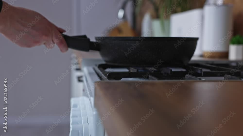 The beginning of cooking, on a white gas kitchen stove with a cast iron black grate, a fire is burning at one burner, a hand puts a black frying pan on it, side view against the background of a white The beginning of cooking, on a white gas kitchen stove with a cast iron black grate, a fire is burning at one burner, a hand puts a black frying pan on it, side view against the background of a white