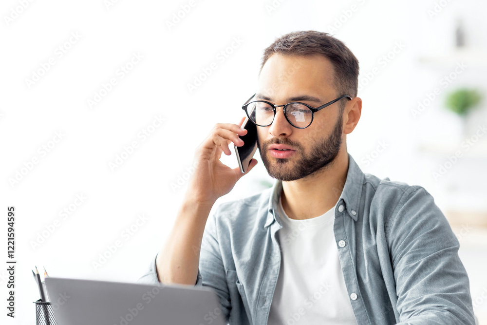 Portrait of happy young guy using laptop, speaking on cellphone, having freelance job at home. Millennial man communicating remotely, having phone call during online business meeting Portrait of happy young guy using laptop, speaking on cellphone, having freelance job at home. Millennial man communicating remotely, having phone call during online business meeting