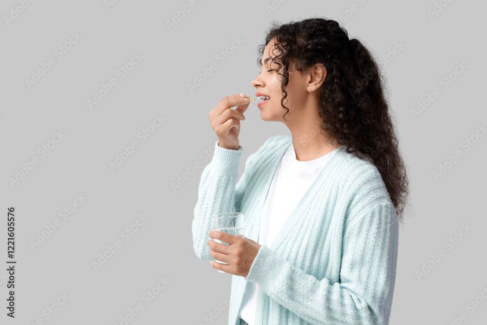 Young African-American woman taking fish oil on grey background Young African-American woman taking fish oil on grey background